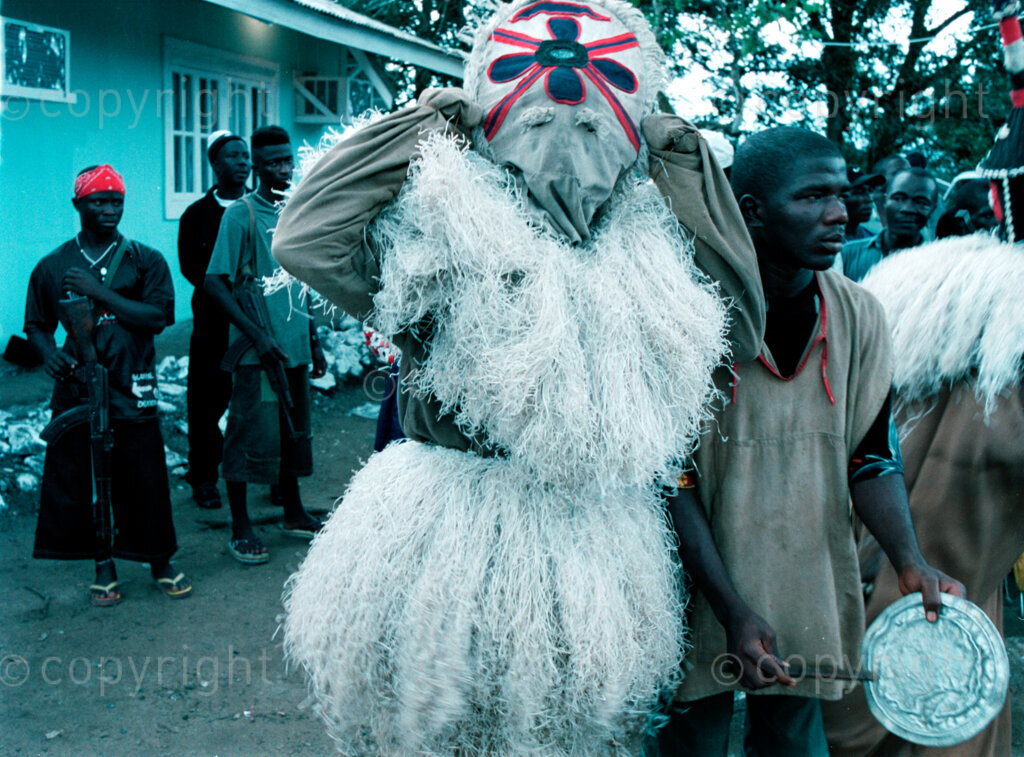 IPMG0954 Tubmanburg, Liberia. LURD rebels watch a traditional dance by masked Lorma dancers for Sekouh Conneh Jr at the town of Tubmanburg, Sept 22, 2003. Liberia's decades long civil conflict has destabilised the entire region and turned a generation of youth into fighters.  Greg Marinovich/South Photographs