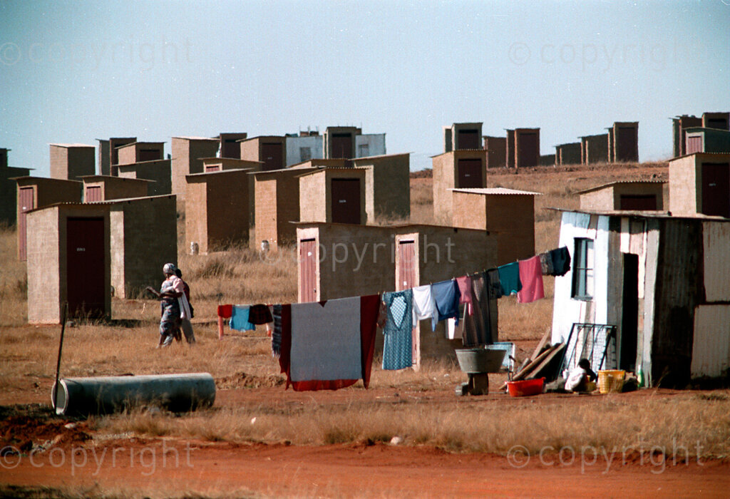 IPMG0344 South Africa, Kagiso, 1995: Women walk through an area marked by toilets and a shack in a new basic housing development by the government near Kagiso township west of Johannesburg, South Africa, 1995.  The South African government's housing policy and subsidies made it possible for them to get a low-cost housing unit on land they now own title deed to.
Photograph by Greg Marinovich/african.pictures