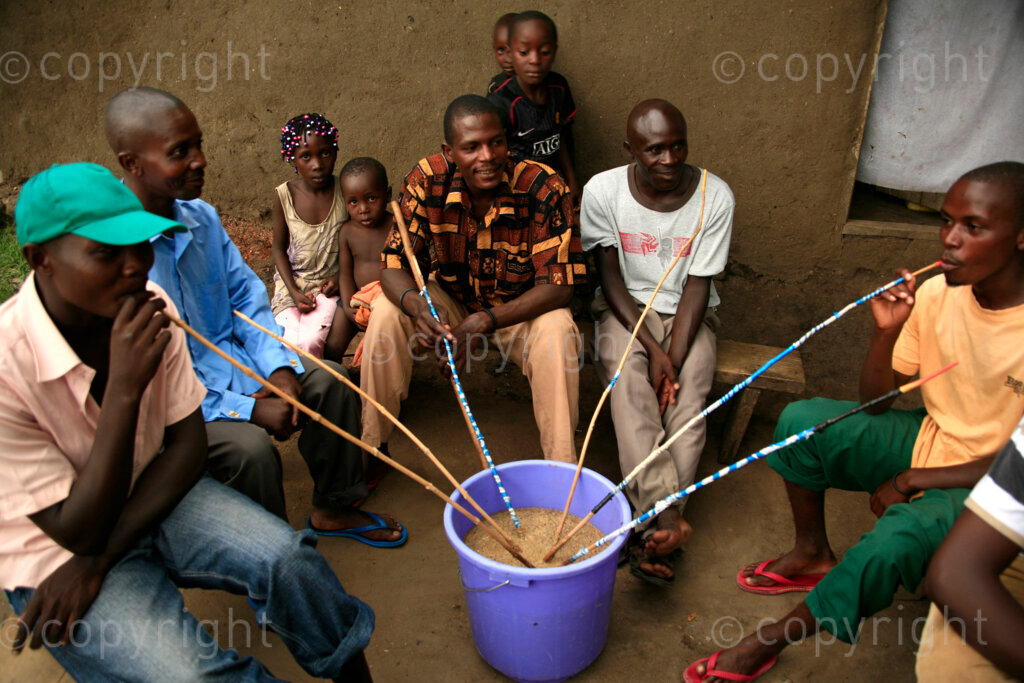African men women and children in the fishing village of Kahendero near Lake George in Uganda sit around drinking from the communal bucket of local brew called marwa which is made by fermenting millet. 
