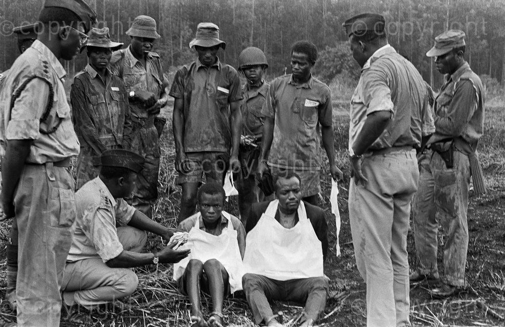 MBALE, UGANDA - FEBRUARY - A crowd of twenty-thousand Ugandans, including women and children, watched from a stadium during a pouring rain as a firing squad prepared for execution two alleged guerrillas from Bugsihu, Sebastino Namirundu, left, and Tom Masaba, a former captain in the Ugandan Army, Mbale, February 1973. Masaba and Namirundu were interrogated, stripped naked, fitted with short white aprons and tied to their execution posts. Masaba, who was accused of being a terrorist, was reported to have said,