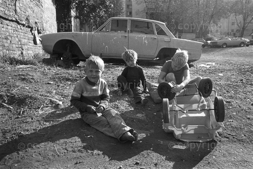 Three young boys repair a toy car in a Hillbrow car lot