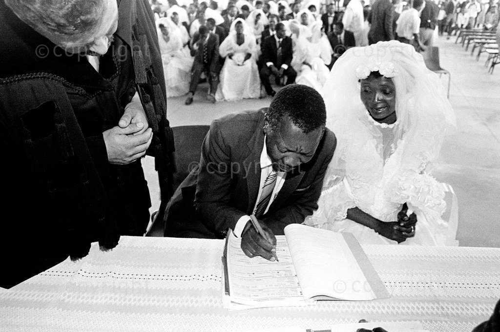 A newly wed couple sign marriage certificates during a mass wedding ceremony held for 36 couples, Schmidtsdrift, South Africa, 1992