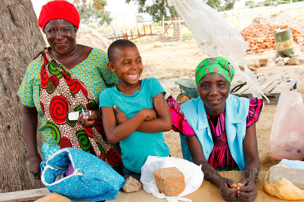 Ovambo women sell sweets and vegetables at a road side stall near Divundu in the Kavango region of Namibia. Informal traders such as them make a living from cash crops like tomatoes and potatoes. The boy goes to school in the afternoon. Local schools are too full to accommodate both primary and high school children so the teenagers go in the morning, while primary school kids attend school in the afternoon.