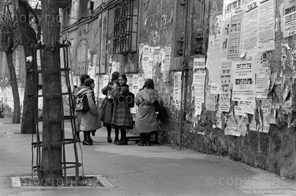 Israel, 1987-1994. A group of young school girls walking in their winter coats alongside a poster-covered wall in Israel. 
Photo Credit: Ken Oosterbroek / african.pictures Photo Credit: Ken Oosterbroek / african.pictures
