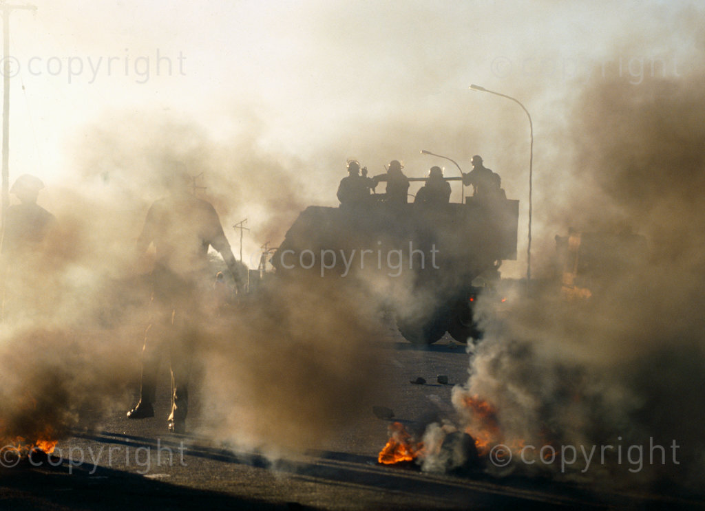 South Africa, 1987-1994. An armoured military vehicle is partially obscured by smoke and flames rising from burning barricades.
Photo Credit: Ken Oosterbroek / african.pictures Photo Credit: Ken Oosterbroek / african.pictures