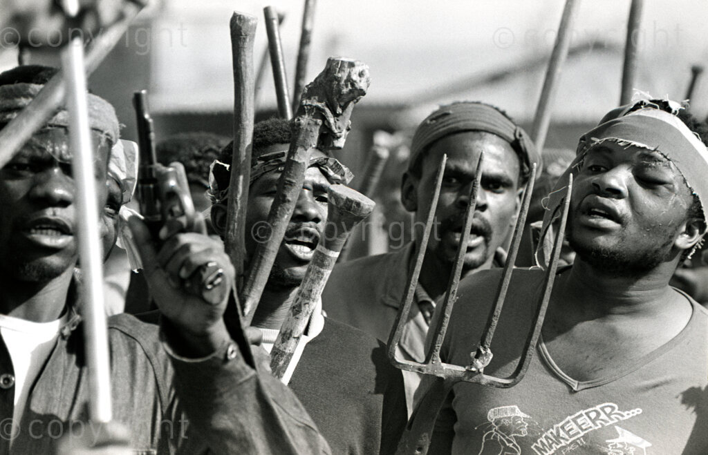 South Africa, 1987-1994. Men, armed with traditional weapons, and some in traditional clothes, dance and chant as they run down the road.
Photo Credit: Ken Oosterbroek / african.pictures Photo Credit: Ken Oosterbroek / african.pictures