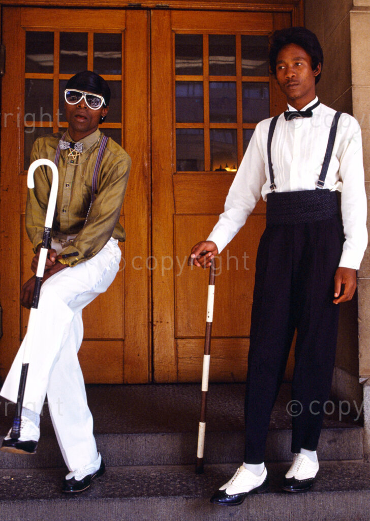 Two smart pantsula dancers show off their clothes.
Pantsula is a highly energetic dance form that originated in the black townships of South Africa during Apartheid. In the 80s and 90s it began to develop more political overtones and became an expression of resistance during the political struggle. Both the dance style and clothing were influenced by 1930s American jazz. Pantsula is Zulu for ‘waddling like a duck’.
Photo Credit: Ken Oosterbroek / african.pictures