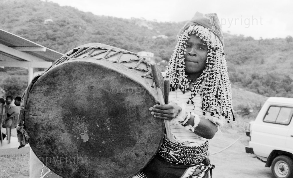 Black and white photo of sangoma in headdress playing a drum; Zulu traditional healers talk about their work in plant conservation and primary health care including AIDS, Zululand, South Africa; documentary; 1998