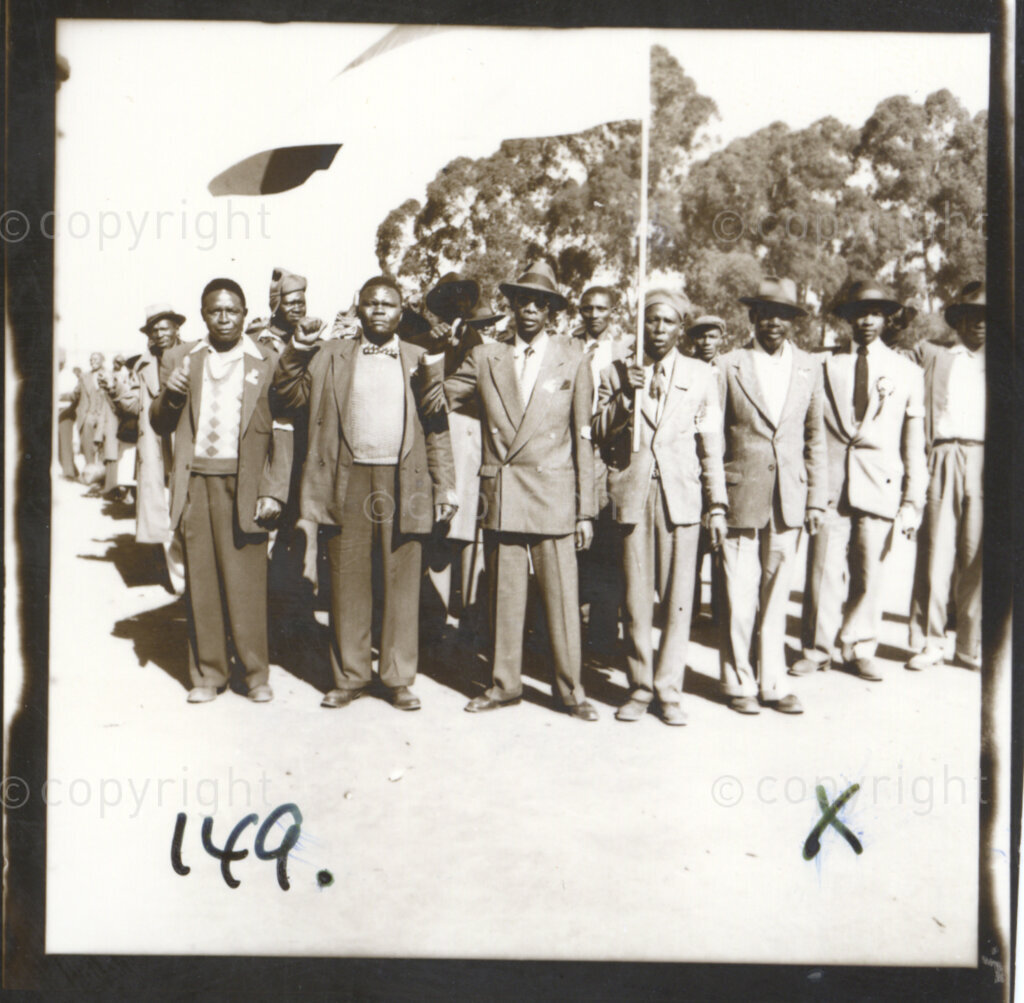 Kliptown, Johannesburg, Transvaal (now Gauteng), South Africa, 19550625. PHOTO: Eli Weinberg.
A group of men holding a flag make the thumbs up salute the sign for unity initiated by the African National Congress (ANC) in the Cape in 1949. They are delegates attending the Congress of the People held in Kliptown, Johannesburg on June 25 and 26 1955. The Freedom Charter was adopted at this Congress.