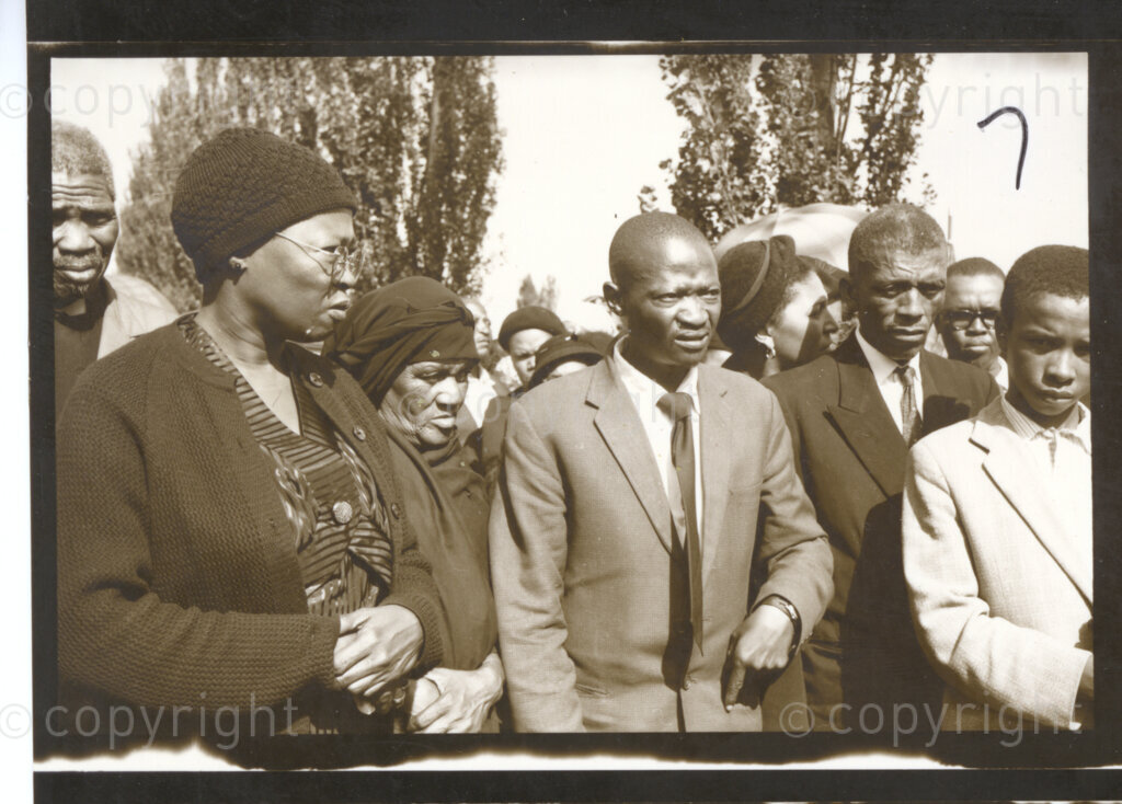 Western Native Township, Johannesburg, Transvaal (now Gauteng), South Africa, 19600101. PHOTO: Eli Weinberg.

A group of people stand together at what may be the funeral of Ida Fiyo Mntwana (1903-1960), former president of the African National Congress Women's League (ANCWL) and a former National President of the Federation of South African Women (FEDSAW) at a cemetery near the Western Native Township, Johannesburg. Ida Mntwana died during the Treason Trial and meetings and demonstrations were banned at the time, but the African National Congress (ANC) decided to make Ida's funeral an occasion for the defiance of the law. Winnie Mandikizela-Mandela (26/9/36-2/4/2018) and other ANCWL leaders were pallbearers at this funeral, but are not visible in the image. The Treason Trial was a trial in Johannesburg in which one hundred and fifty-six people were arrested in a raid and accused of treason in South Africa in 1956. The main trial lasted until 1961 when all of the defendants were found not guilty.