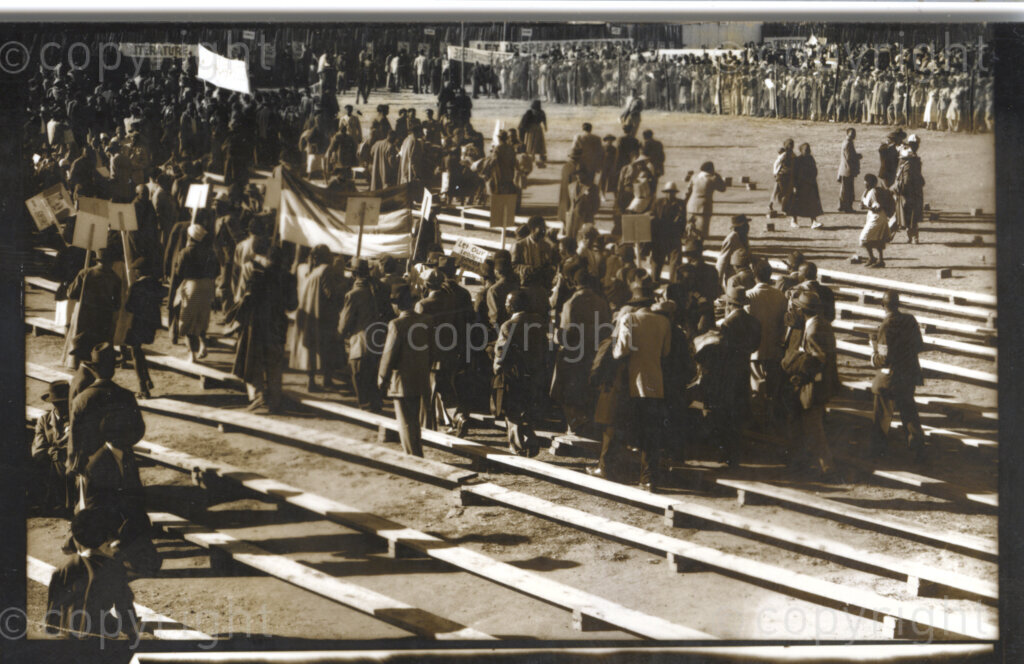 Kliptown, Johannesburg, Transvaal (now Gauteng), South Africa, 19550625. PHOTO: Eli Weinberg.
A large group of people walk around during the Congress of the People held in Kliptown, Johannesburg on the 25 and 26 June 1955. They carry flags, banners and placards. Some of the placards read