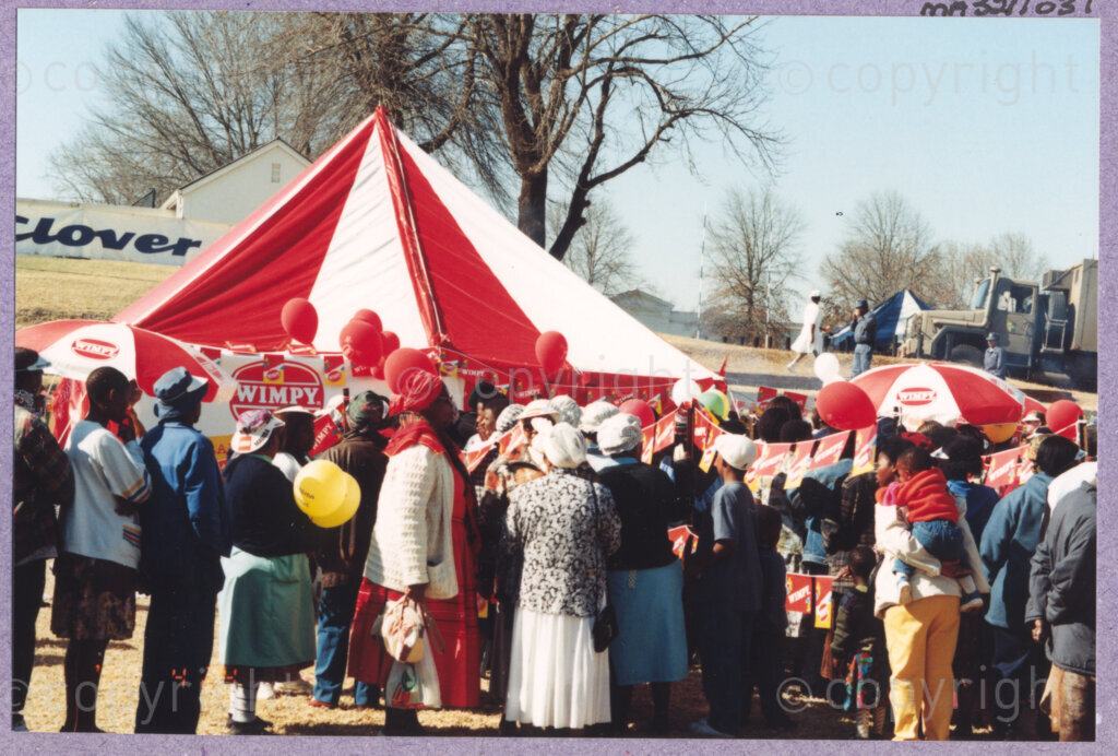 Hilton College, Pietermaritzburg, KwaZulu-Natal, South Africa, 19960717. PHOTO: ANC Archives.

People gather outside a Wimpy tent that is serving party food at the 78th birthday celebration of the President of South Africa, Nelson Mandela. More than 2,000 children who are living with disability in disadvantaged communities across the county have been invited to the day-long birthday extravaganza being held on the 17th July 1996 on the grounds of Hilton College near Pietermaritzburg in the KwaZulu-Natal Midlands. The children, their carers, Madiba and other guests are being entertained playing games, enjoying party fare, and attending a circus performance in a big top (a first-time experience for Madiba who has, to date, never been to a circus!). The event has the backing of the Nelson Mandela Children's Fund.