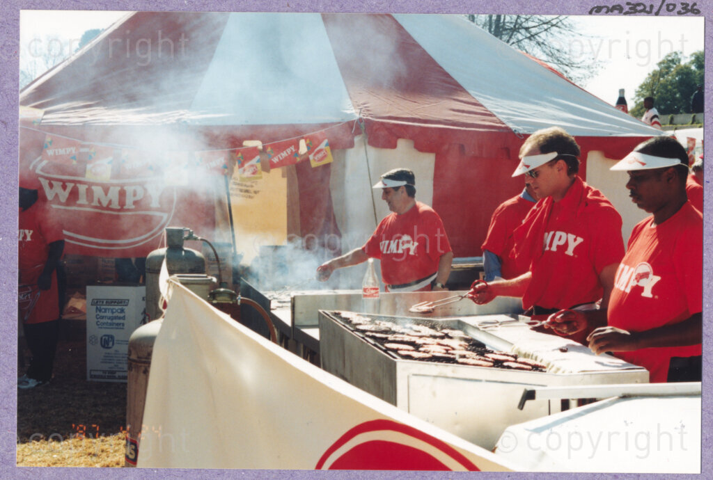 Hilton College, Pietermaritzburg, KwaZulu-Natal, South Africa, 19960717. PHOTO: ANC Archives.

Employees of Wimpy wearing red T-shirts grill hamburgers in an outdoor kitchen at the 78th birthday celebration of the President of South Africa, Nelson Mandela who is fondly known as Madiba. More than 2,000 children who are living with disability in disadvantaged communities across the county were invited to the day-long birthday extravaganza being held on the 17th July 1996 on the grounds of Hilton College near Pietermaritzburg in the KwaZulu-Natal Midlands. The children, their carers, Madiba and other guests are being entertained playing games, enjoying party fare, and attending a circus performance in a big top (a first-time experience for Madiba who has, to date, never been to a circus!). The event has the backing of the Nelson Mandela Children's Fund.