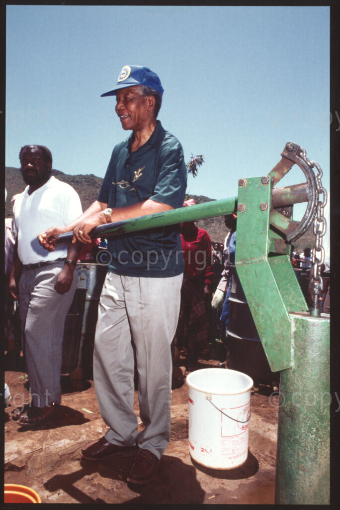 Maila Mapitsane village , Sekhukhuneland, Transvaal, South Africa, 19921130. PHOTO: ANC Archives.

Frans Themba, Operation Hunger senior relief field worker (left) looks on as the African National Congress President, Nelson Mandela (centre) works the water pump at the Makua Garden in the Maila Mapitsane village in the Sekhukhuneland region in November 1992.