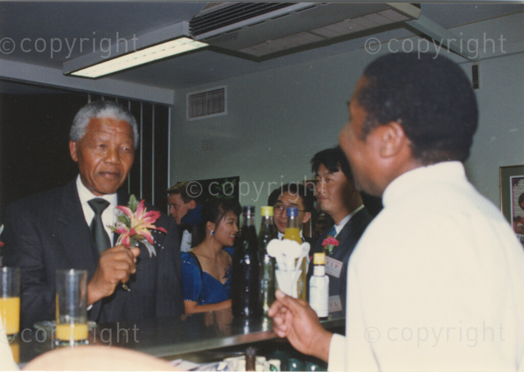 Parktonian Hotel, Johannesburg, Transvaal, South Africa, 19940309. PHOTO: ANC Archives.

The President of the African National Congress (ANC), Nelson Mandela (left) in conversation with the barman at an ANC voter education fund-raising dinner hosted by the Taiwanese community in South Africa on the 9 March 1994. Leading up to the 1994 elections in South Africa, Taiwan embarked on a public relations campaign in efforts to improve relations with the ANC, providing financial support to the ANC's election campaign. South Africa's diplomatic ties with Taiwan (The Republic of China) ended in 1998 however when Nelson Mandela, as President of South Africa, recognized the People's Republic of China.