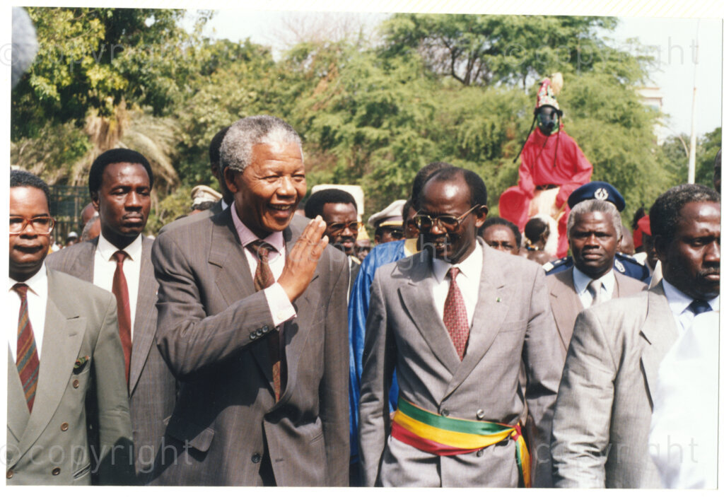 Senegal, 19920601. PHOTO: ANC Archives.

A photo of many people on a walkabout with Nelson Mandela (center) waving at the crowd during his visit to Senegal in June 1992.