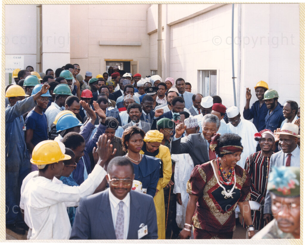 Kaduna Refinery, Kaduna, Kaduna, Nigeria, 19900515. PHOTO: ANC Archives.

Nelson Mandela, with his fist raised, walks behind Winnie Madikizela-Mandela, as they are cheered by a crowd during their visit to Kaduna Refinery, Nigeria, 15 May 1990.