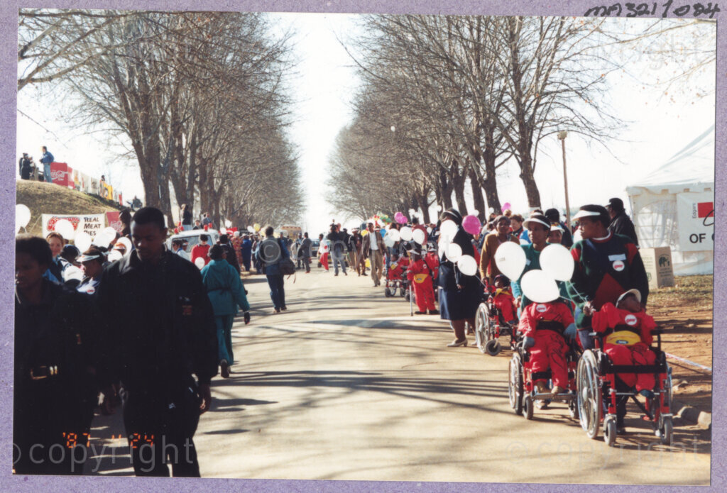Hilton College, Pietermaritzburg, KwaZulu-Natal, South Africa, 19960717. PHOTO: ANC Archives.

Children in wheelchairs and dressed in new, red outfits that they have been given, are accompanied by their carers to the 78th birthday celebration of the President of South Africa, Nelson Mandela. More than 2,000 children who are living with disability in disadvantaged communities across the county have been invited to the day-long birthday extravaganza being held on the 17th July 1996 on the grounds of Hilton College near Pietermaritzburg in the KwaZulu-Natal Midlands. In advance of today's festivities, the invited children have been examined and treated by a team of orthopaedic specialists and physiotherapists. Many of them have been given life-changing wheelchairs. The event has the backing of the Nelson Mandela Children's Fund. Nelson Mandela was born on the 18th July 1918 in Mvezo, a small village in the Eastern Cape.