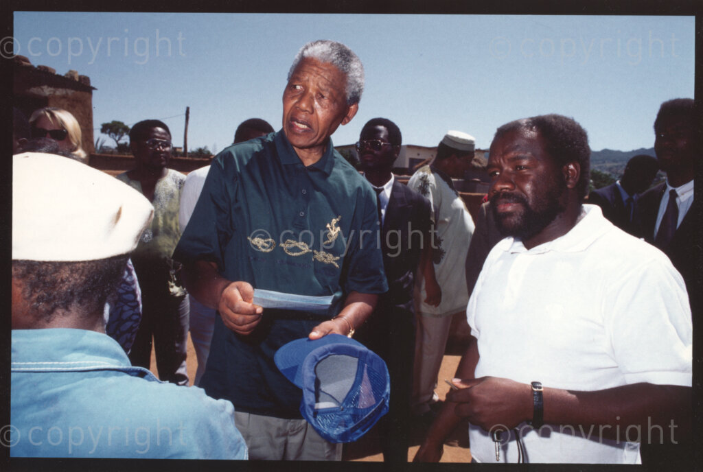 Tsehlwaneng village, Sekhukhuneland, Transvaal, South Africa, 19921130. PHOTO: ANC Archives.

The President of the African National Congress, Nelson Mandela (centre), and Frans Themba (right), an Operation Hunger senior relief field worker, visit community members in Tsehlwaneng village in the Sekhukhuneland region in November 1992.