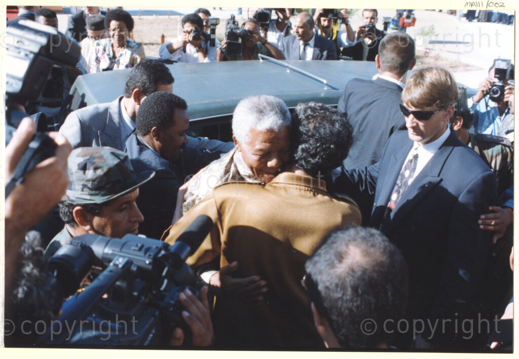 Tripoli, Tripoli District , Great Socialist People's Libyan Arab Jamahiriya (Libyan Arab Republic) , 19971022. PHOTO: ANC Archives.

Nelson Mandela (centre, with one of his bodyguards in attendance) warmly embraces his host Libyan leader Muammar Mohammed Abu Minyar Gaddafi (foreground) upon his arrival in Tripoli, Libya (officially the Great Socialist People's Libyan Arab Jamahiriya (Libyan Arab Republic)) on 22 October 1997. This is the second official visit as president of South Africa that Mandela has made to Libya, the first being in 1994, shortly after the first democratic elections. Libya has been an ally to the anti-apartheid movements since Colonel Muammar Gaddafi came to power in 1969, providing funding and support to the African National Congress (ANC). South Africa bestowed the Order of Good Hope, one of its highest honours, on Muammar Gaddafi in 1997.