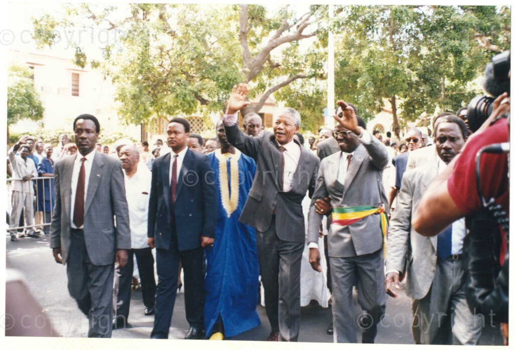 Senegal, 19920601. PHOTO: ANC Archives.

A group photo of many people with Nelson Mandela (front, first from left) waving at the crowd and Alfred Nzo (third row, first from left with the white shirt) during Mandela's official visit to Senegal in June 1992.