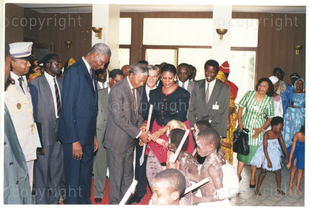 Senegal, 19920601. PHOTO: ANC Archives.

Nelson Mandela (centre) is seen standing next to Abdou Diouf (left from Mandela), greeting children in traditional costume, during Mandela's visit to Senegal in June 1992.