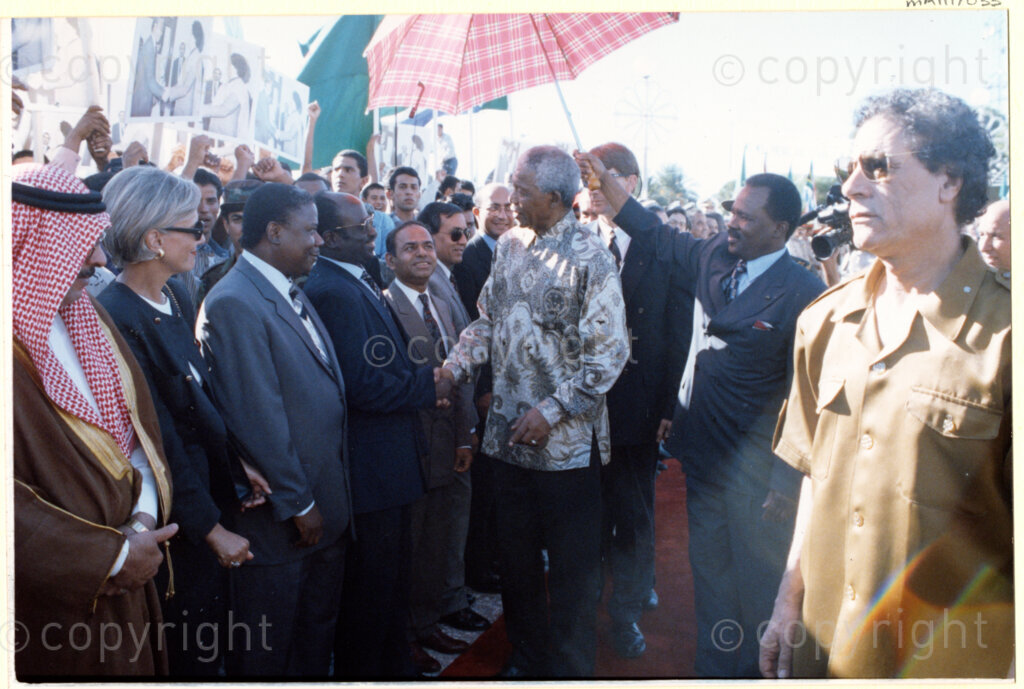 Tripoli, Tripoli District , Great Socialist People's Libyan Arab Jamahiriya (Libyan Arab Republic) , 19971022. PHOTO: ANC Archives.

Nelson Mandela (centre), accompanied by his host Libyan leader Muammar Mohammed Abu Minyar Gaddafi (right), greets Libyan officials who have lined up to meet him in Tripoli, Libya (officially the Great Socialist People's Libyan Arab Jamahiriya (Libyan Arab Republic)) on 22 October 1997. This is the second official visit as president of South Africa that Mandela has made to Libya, the first being in 1994, shortly after the first democratic elections. Libya has been an ally to the anti-apartheid movements since Colonel Muammar Gaddafi came to power in 1969, providing funding and support to the African National Congress (ANC). South Africa bestowed the Order of Good Hope, one of its highest honours, on Gaddafi in 1997.