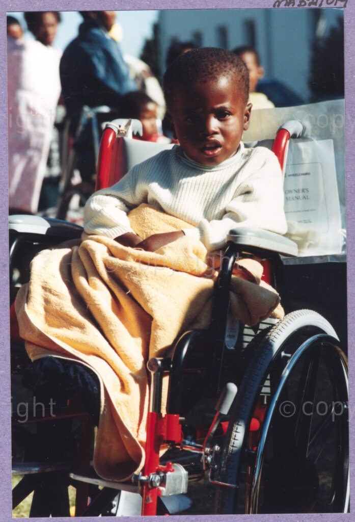 Hilton College, Pietermaritzburg, KwaZulu-Natal, South Africa, 19960717. PHOTO: ANC Archives.

A young child wrapped warmly, rests in his new wheelchair at the 78th birthday celebration of the President of South Africa, Nelson Mandela, fondly known as Madiba. More than 2,000 children who are living with disability in disadvantaged communities across the county have been invited to the day-long birthday extravaganza being held on the 17th July 1996 on the grounds of Hilton College near Pietermaritzburg in the KwaZulu-Natal Midlands. In advance of today's festivities, the invited children have been examined and treated by a team of orthopaedic specialists and physiotherapists. Like this young child, many of them have been given life-changing wheelchairs. The event has the backing of the Nelson Mandela Children's Fund. Nelson Mandela was born on the 18th July 1918 in Mvezo, a small village in the Eastern Cape.