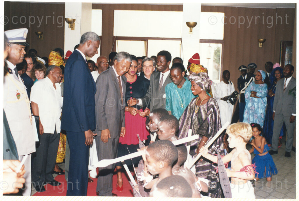 Senegal, 19920601. PHOTO: ANC Archives.

A photo of many people with Nelson Mandela (second from left),Senegalese President, Abdou Diouf (first from left), and Alfred Nzo (second row, second from left, with the white shirt), being welcomed by children in traditional clothing, during Mandela's official visit to Senegal in June 1992.