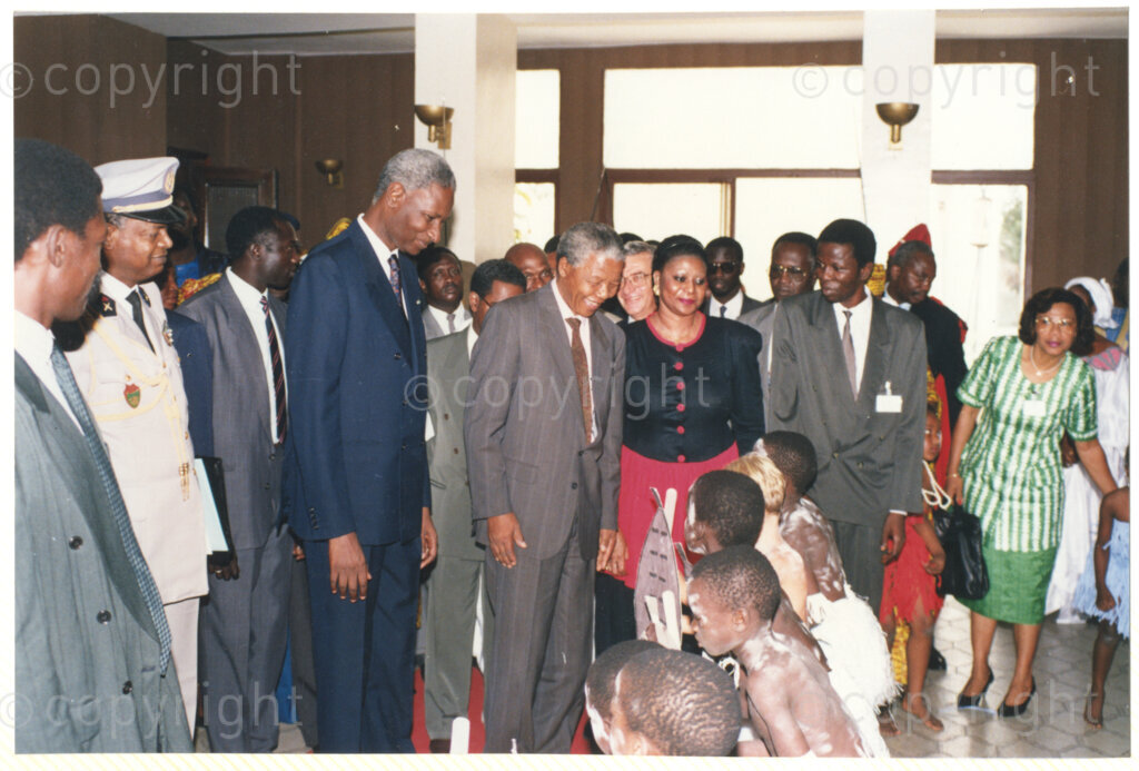 Senegal, 19920601. PHOTO: ANC Archives.

Nelson Mandela (center) is seen standing next to Abdou Diouf (left from Mandela), greeting children in traditional costumes, during his visit to Senegal in June 1992.