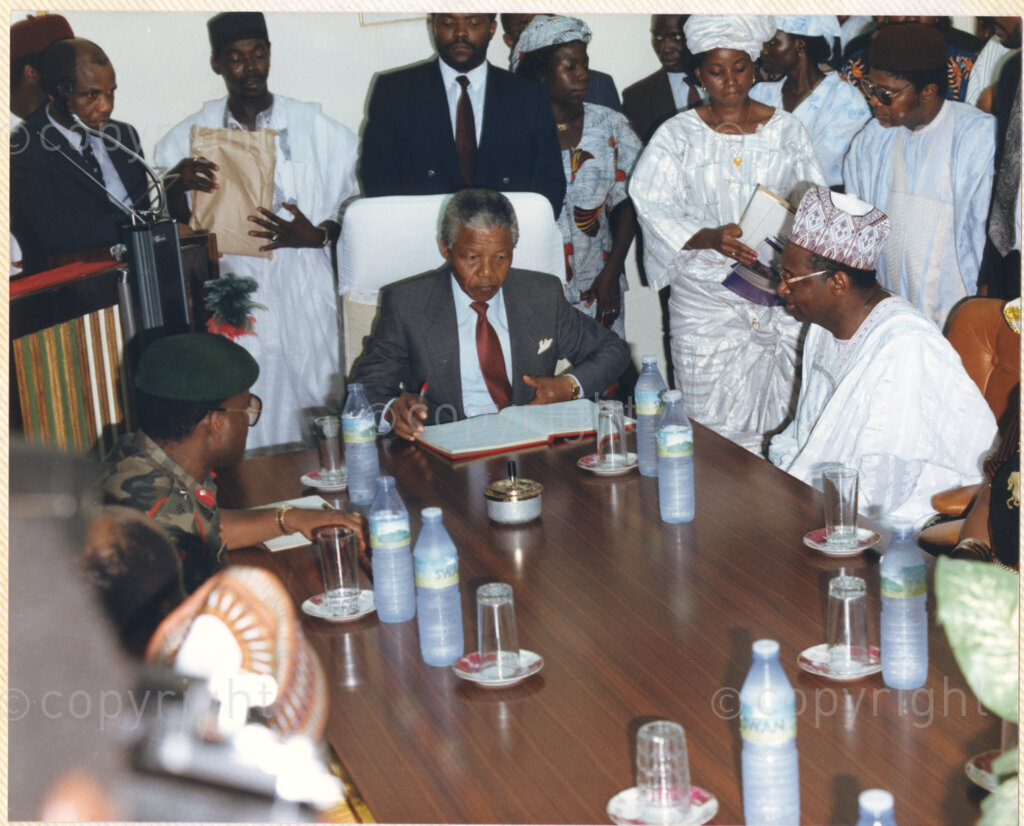 Kaduna Refinery, Kaduna, Kaduna, Nigeria, 19900515. PHOTO: ANC Archives.

Nelson Mandela (seated center) signs a document as various unidentified officials look on during his visit to Kaduna Refinery, Nigeria, 15 May 1990.