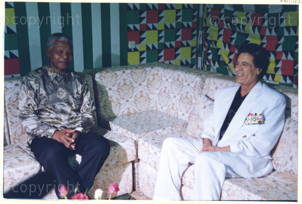 Tripoli, Tripoli District , Great Socialist People's Libyan Arab Jamahiriya (Libyan Arab Republic), 19971022. PHOTO: ANC Archives.

Nelson Mandela is seated left of his host Libyan leader Muammar Mohammed Abu Minyar Gaddafi at a social function in Tripoli, Libya (officially the Great Socialist People's Libyan Arab Jamahiriya (Libyan Arab Republic)) on 22 October 1997. This is the second official visit as president of South Africa that Mandela has made to Libya, the first being in 1994, shortly after the first democratic elections. Libya has been an ally to the anti-apartheid movements since Colonel Muammar Gaddafi came to power in 1969, providing funding and support to the African National Congress. South Africa bestowed the Order of Good Hope, one of its highest honours, on Gaddafi in 1997.