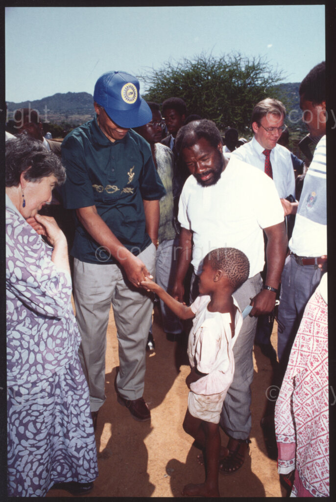 Tsehlwaneng village, Sekhukhuneland, Transvaal, South Africa, 19921130. PHOTO: ANC Archives.

The President of the African National Congress (ANC), Nelson Mandela (second left) shakes hands with a small child in Tshehlwaneng village, Sekhukhuneland while Executive Director of Operation Hunger, Ina Perlman (left), and Frans Themba, an Operation Hunger senior relief field worker (right) look on in November 1992.