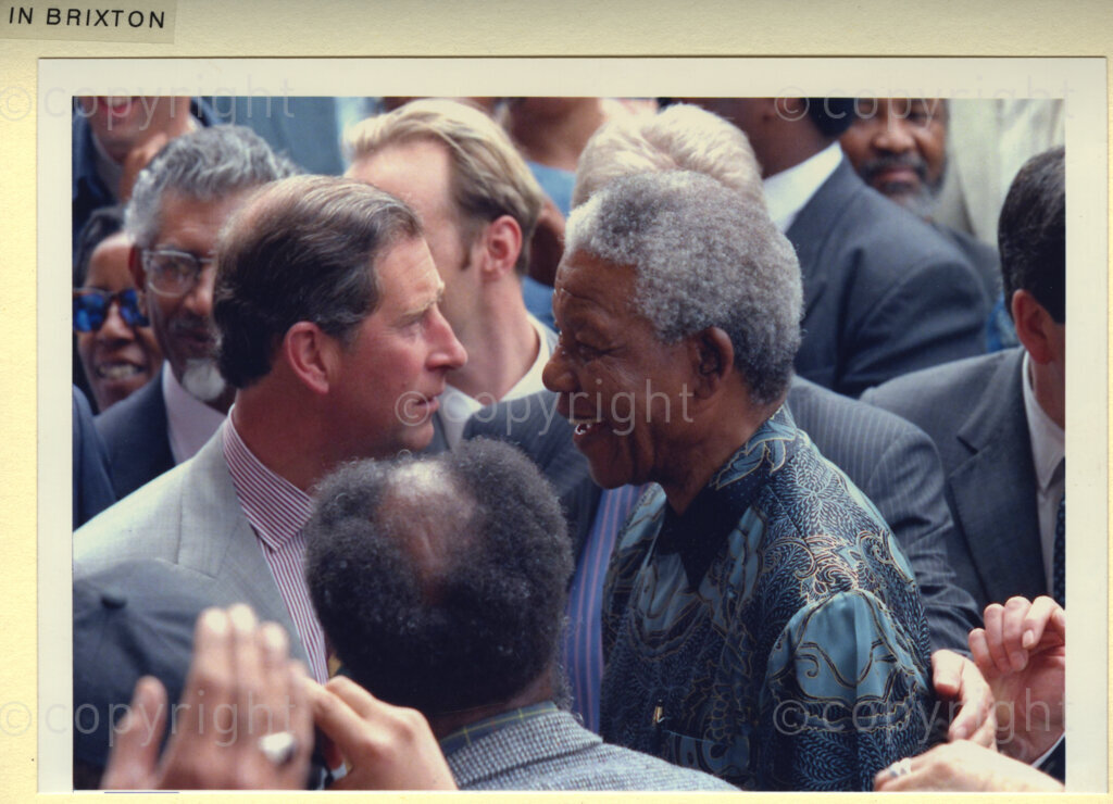 Brixton, London, United Kingdom, 19960701. PHOTO: ANC Archives: President Nelson Mandela is on a state visit to the United Kingdom, in July 1996. He is seen here, face to face in conversation with Prince Charles. (Immediately behind Prince Charles, is Mac Maharaj.) All three are standing in the midst of a jubilant crowd in Brixton, a predominantly black neighbourhood in London. These people revere Mandela for the work he has done to overcome racism in South Africa. His welcome is tumultuous.