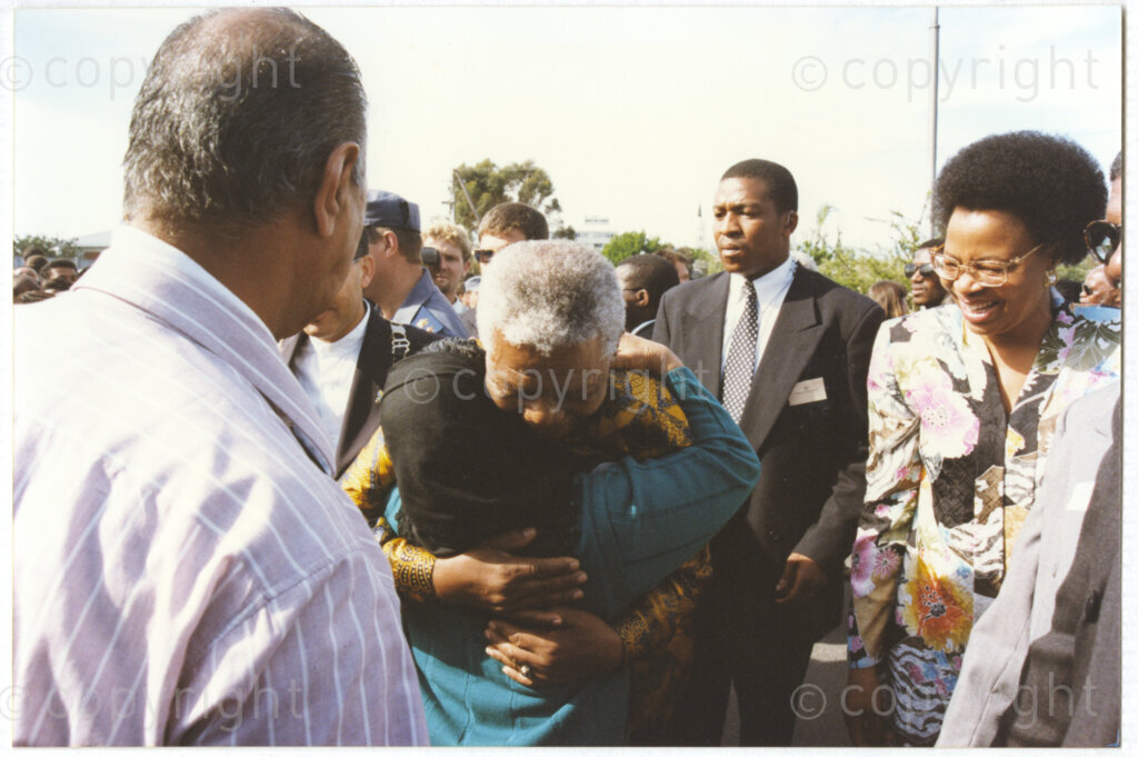 Worcester Railway Station, Worcester, Western Cape, Republic of South Africa, 19970927. PHOTO: ANC Archives.

When the relaunched luxury Blue Train stopped in Worcester, Western Cape on 27 September 1997 President Nelson Mandela was delighted to meet an old friend, Ayesha (Bibi) Dawood and her husband Yusuf Mukuddam. She was an ANC member and political activist and had like Mandela been tried for treason in 1956 and had later gone into exile. Nelson Mandela gives the tiny Bibi Mukuddam a big hug, while her husband Yusuf Mukuddam (left), and Graca Machel (right) look on.