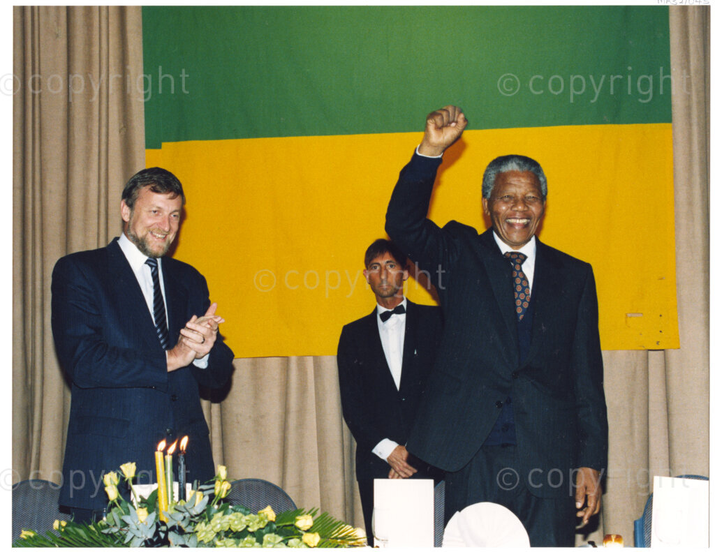 Australia, October 1990. PHOTO: ANC Archives: Raising the solidarity salute, Nelson Mandela stands proudly in front of the African National Congress flag. On this 1990 visit to Australia he addresses many eager audiences, all of whom marvel at Mandela's determination and resilience following a 27 year stretch in prison. Mandela comments that he had to banish bitterness in order to be truly free from prison. Monday 22 October to Saturday 27 October 1990.