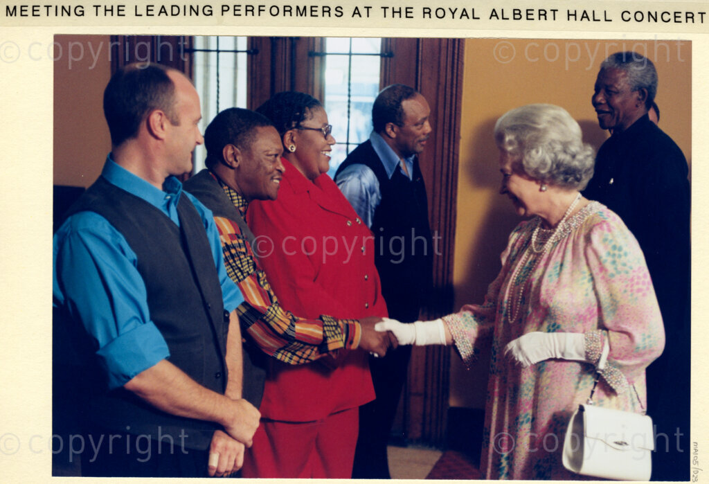 Back stage at the Royal Albert Hall, London, United Kingdom, 19960701. PHOTO: ANC Archives: During his state visit to the United Kingdom in July 1996, President Nelson Mandela attends a concert with Queen Elizabeth II at the Royal Albert Hall. After the show, Mandela and the Queen, (right), meet and greet the performers. Amongst these shown in the image are Quincy Jones and Hugh Masekela. Other performers that night, include the Ladysmith Black Mambazo, Phil Collins and Tony Bennett.