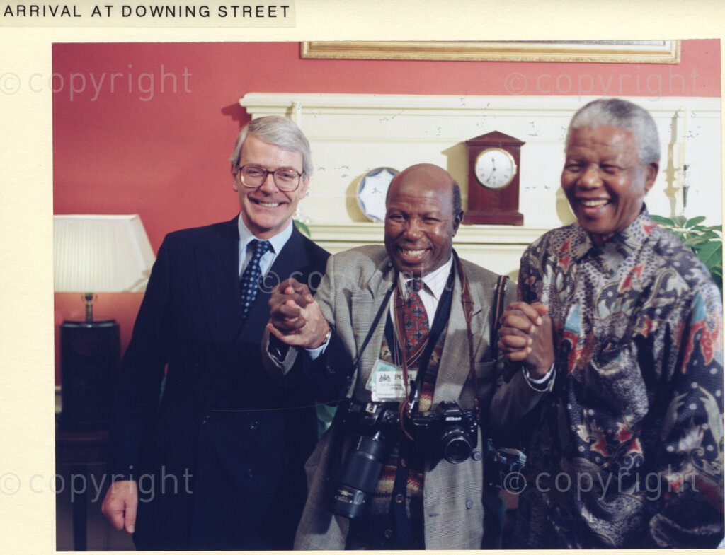 Downing Street, London, United Kingdom, 19960701. PHOTO: ANC Archives: In July 1996, South African President, Nelson Mandela goes on a state visit to the United Kingdom. He is seen here with British Prime Minister, John Major, (on the left), and an unknown man standing between himself and Major. This man appears to be a photographer. All three men are in high spirits.