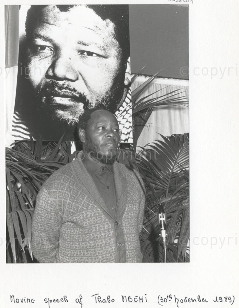 Arcueil, Val-de-Marne, Paris, Île-de-France, France, 19891130. PHOTO: ANC Archives: An African National Congress (ANC) comrade, standing in front of a large poster of Nelson Mandela, makes a moving speech at a function in Arcueil, France on 30 November 1989 to commemorate Dulcie September, and in solidarity with Nelson Mandela who is imprisoned in South Africa. Dulcie September, a South African anti-apartheid activist and the Chief Representative of the ANC in France, Switzerland and Luxembourg, was assassinated outside the ANC's Paris office at 28 Rue des Petites-Ecuries last year on 29 March 1988.