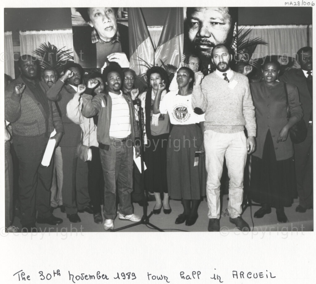 Arcueil, Val-de-Marne, Paris, Île-de-France, France, 19891130. PHOTO: ANC Archives: African National Congress comrades living in exile including Trevor Manuel (second right) and members of various French anti-apartheid movements gather in Arcueil, France on 30 November 1989 for the unveiling of a commemorative plaque for Dulcie September. Behind the group are posters of Nelson Mandela (right) and Dulcie September (left). Dulcie September, a South African anti-apartheid activist and ANC Chief Representative in France, Switzerland and Luxembourg, was assassinated outside the ANC's Paris office at 28 Rue des Petites-Ecuries last year on 29 March 1988.