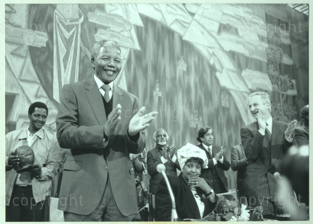 Geneva Ecumenical Centre, Geneva, Switzerland, 19900601. PHOTO: ANC Archives.

A few months after his release from prison, newly elected Deputy President of the African National Congress (ANC) Nelson Mandela and his wife, Winnie Madikizela-Mandela make an official visit to Switzerland, 4-9 June 1990. Shortly after his arrival in Geneva, he visits staff and officials and representatives of the World Council of Churches (WCC) at the Geneva Ecumenical Centre. Surrounded by dignitaries and officials on the stage, Nelson Mandela (front left) applauds while Winnie Madikizela-Mandela remains seated.