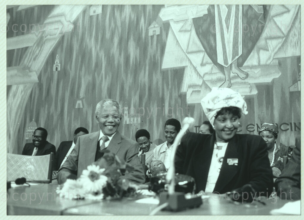 Geneva Ecumenical Centre, Geneva, Switzerland, 19900601. PHOTO: ANC Archives.

Seated at the main table on stage recently elected Deputy President of the African National Congress (ANC) Nelson Mandela (left) and Winnie Madikizela-Mandela smile broadly amongst unidentified officials at the Geneva Ecumenical Centre, Switzerland when the Mandela couple visit staff, officials and representatives of the World Council of Churches (WCC) at the time of Nelson Mandela's official visit to Switzerland, 4-9 June 1990. During the visit, barely a few months after his release from prison, Nelson Mandela expresses his gratitude to the church for its support of the anti-apartheid struggle.