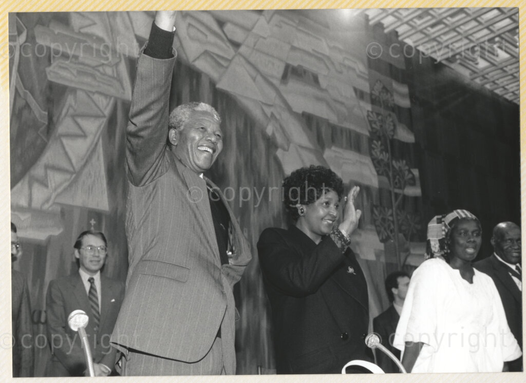 Geneva Ecumenical Centre, Geneva, Switzerland, 19900601. PHOTO: ANC Archives.

Standing on the stage, Winnie Madikizela-Mandela, (second right) and recently elected Deputy President of the African National Congress (ANC) Nelson Mandela (first right) with his right hand held high in the auditorium at the Geneva Ecumenical Centre when the Mandela couple visit the staff, officials and representatives of the World Council of Churches (WCC) during Nelson Mandela's official visit to Switzerland, 4-9 June 1990.
