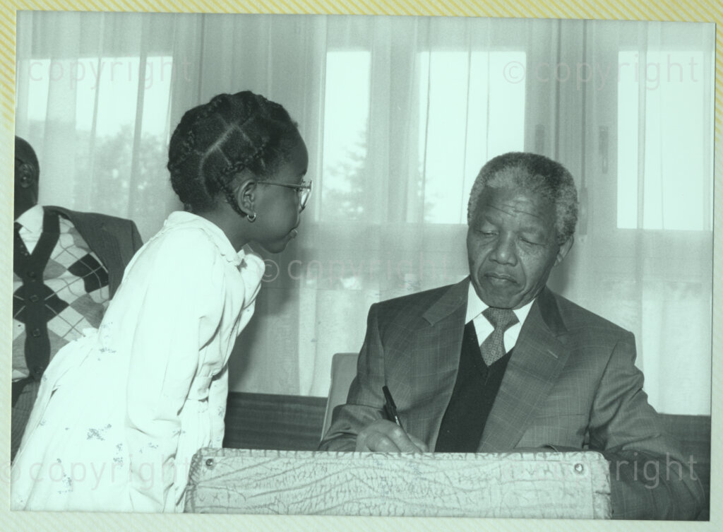 International Reformed Centre John Knox, Geneva, Switzerland, 19900609. PHOTO: ANC Archives.

Recently appointed Deputy President of the African National Congress (ANC) Nelson Mandela (seated) signs an autograph for a young girl Nehanda Mutambirwa at the International Reformed Centre John Knox (IRCJK), Geneva, Switzerland, 9 June 1990 during Nelson Mandela Mandela's official visit to Switzerland, 4-9 June 1990.