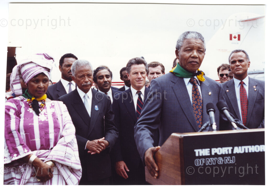 New York, New York State, United States of America, 19900620. PHOTO: ANC Archives.

During Nelson Mandela's Freedom Tour of the United States of America, in June 1990, the core message in each of his speeches in New York, is the need for ongoing financial support of the African National Congress, while at the same time bringing pressure to bear on the apartheid government by maintaining economic, political, cultural and sporting sanctions. Mandela is seen here with an African National Congress bandana around his neck. Winnie wears a traditional African outfit. She stands beside their host, Mayor David Dinkins.