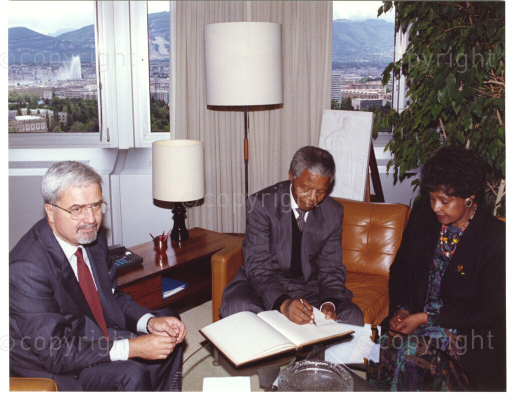 International Labour Organisation, Geneva, Switzerland, 19900608. PHOTO: ANC Archives.

Barely four months after his release from 27 years in prison the deputy president of the African National Congress (ANC), Nelson Mandela and his spouse Winnie Madikizela-Mandela embark on an official visit to Switzerland, 4-9 June 1990. Sitting comfortably in a lounge, paging through a book at the International Labour Organisation (ILO) (left to right) Michel Hansenne the director-general of the ILO, Nelson Mandela who signs a visitors book and Winnie Madikizela-Mandela. On this occasion Nelson Mandela delivers his addresses to the 77th Session of the International Labour Conference (ILC), 8 June 1990 where he expresses his gratitude for the support received from the ILO and urges the international community to persist in their demands that all political prisoners must be released, political trials ended, exiles returned, repressive legislation repealed, and the state of emergency ended in its entirety.