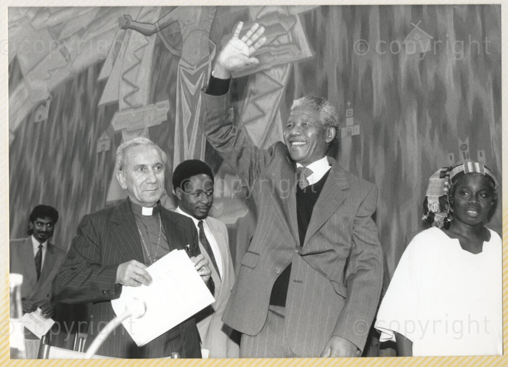 Geneva Ecumenical Centre, Geneva, Switzerland, 19900601. PHOTO: ANC Archives.

Newly elected Deputy President of the African National Congress (ANC) Nelson Mandela (third left) waves at guests from the stage at the Geneva Ecumenical Centre. General Secretary of the World Council of Churches Emilio Castro (first left) and unidentified officials join Nelson Mandela on stage. Barely a few months after his release from prison Nelson Mandela and his wife Winnie Madikizela-Mandela make an official visit to Switzerland, 4-9 June 1990. Shortly after his arrival, he visits staff and officials and representatives of the WCC at the Ecumenical Centre in Geneva.