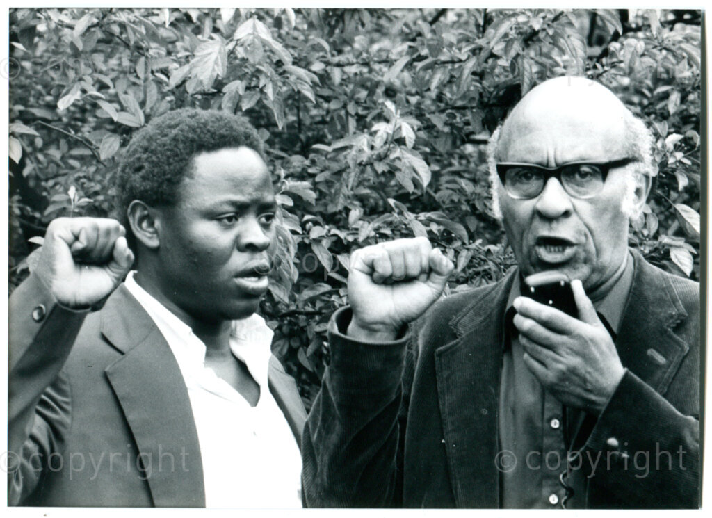James Madhlope Phillips (right; SA trade union leader) sings South African freedom Songs in front of the SA embassy in The Hague with Manala Manzini (left; secretary ANC Youth Section; in 1981-82 Govan Mbeki Fund fellow in Amsterdam) in June 1981. Photographer: Jan Stegeman.