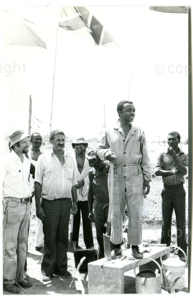 The hoisting of the ANC flag each morning at the start of the working day in Mazimbu, Tanzania, December 1982; in front, from left to right: ?, Oswald Dennis (project supervisor), Tim Maseko (SOMAFCO Principle). Photo: Eli Weinberg Photo Lab.