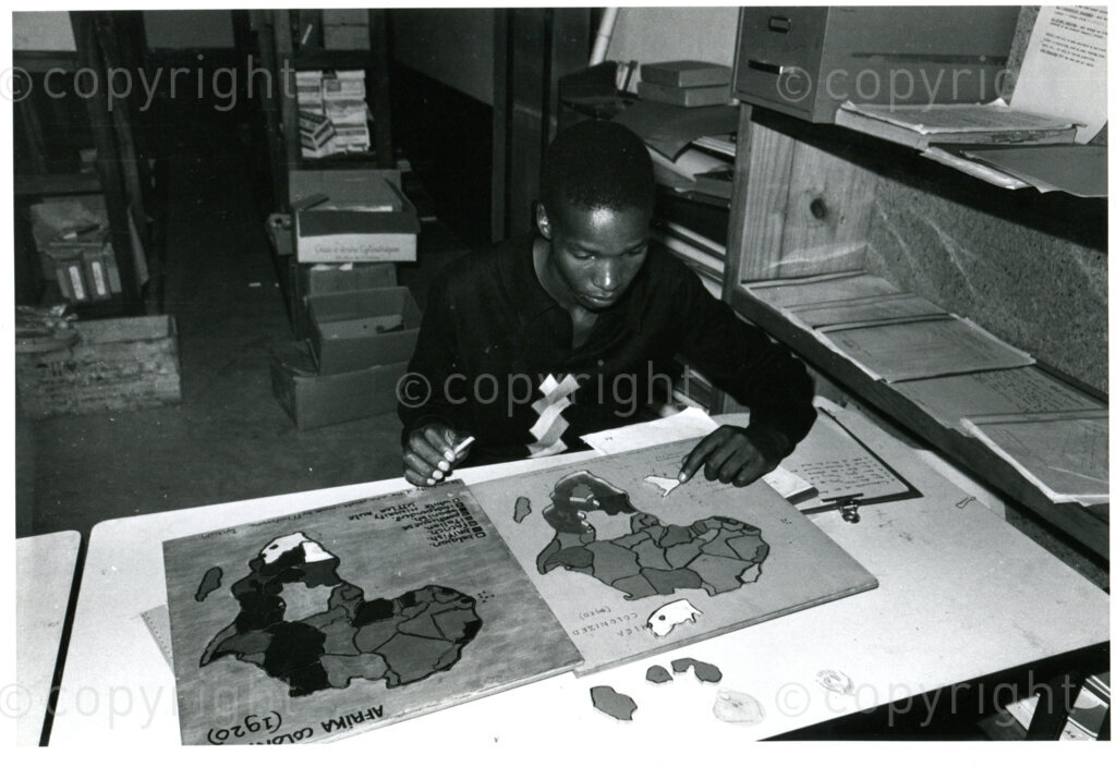 SOMAFCO student putting educational jigsaw puzzle on Africa together  sent by Dutch AAM; Mazimbu, Tanzania, 1983. Photo: Eli Weinberg Photo Lab.